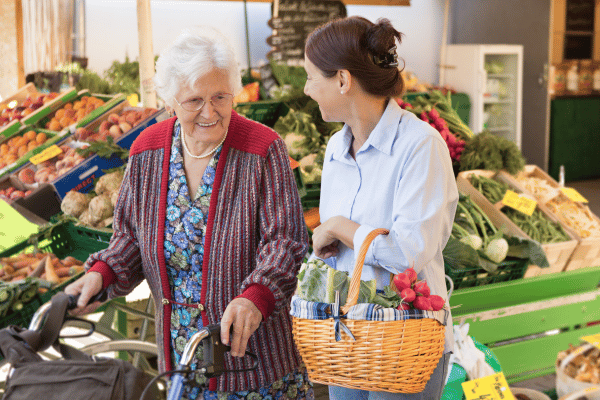 An elderly women walking with another women who is holding a basket of flowers.